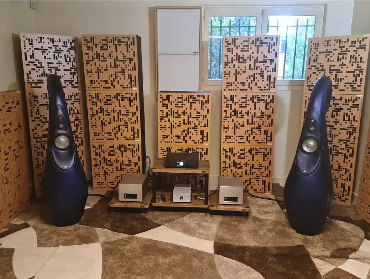 Deux belles enceintes Vivid Audio G2s2 bleues devant des panneaux acoustiques à motifs dans une pièce avec une moquette beige à motifs (par 1877.audio)