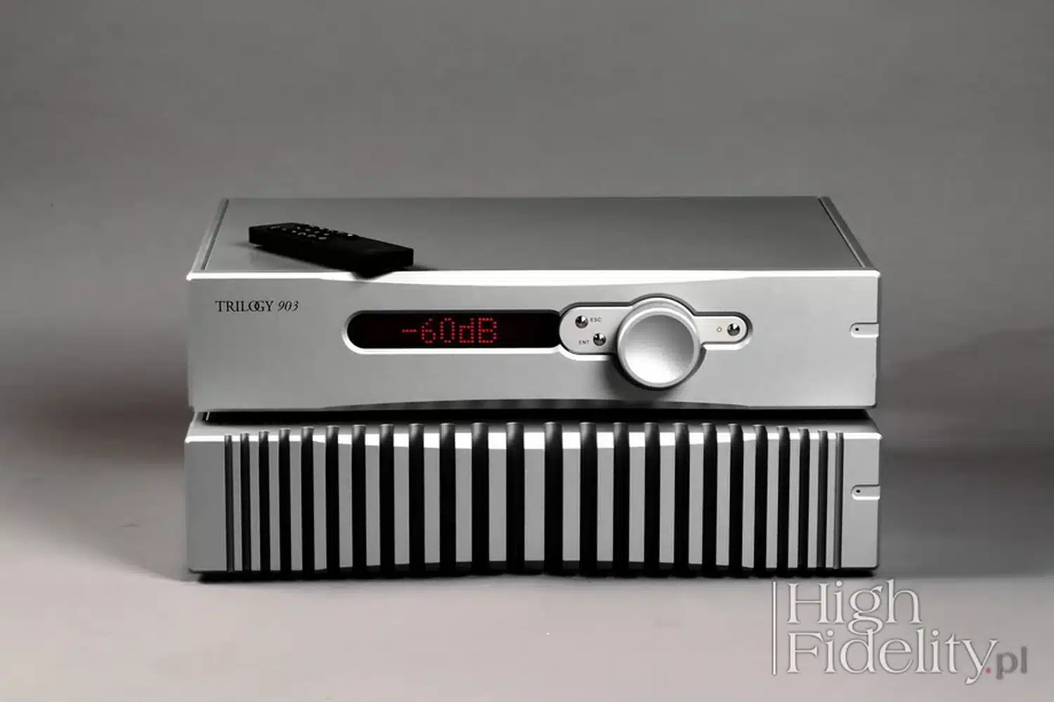 Un préamplificateur audio Trilogy Audio 903 en aluminium argenté avec un affichage numérique indiquant "-60 dB" et sa télécommande sur le dessus posés sur un amplificateur Trilogy Audio 993 avec ses ailettes de refroidissement en premier plan (par 1877.audio)
