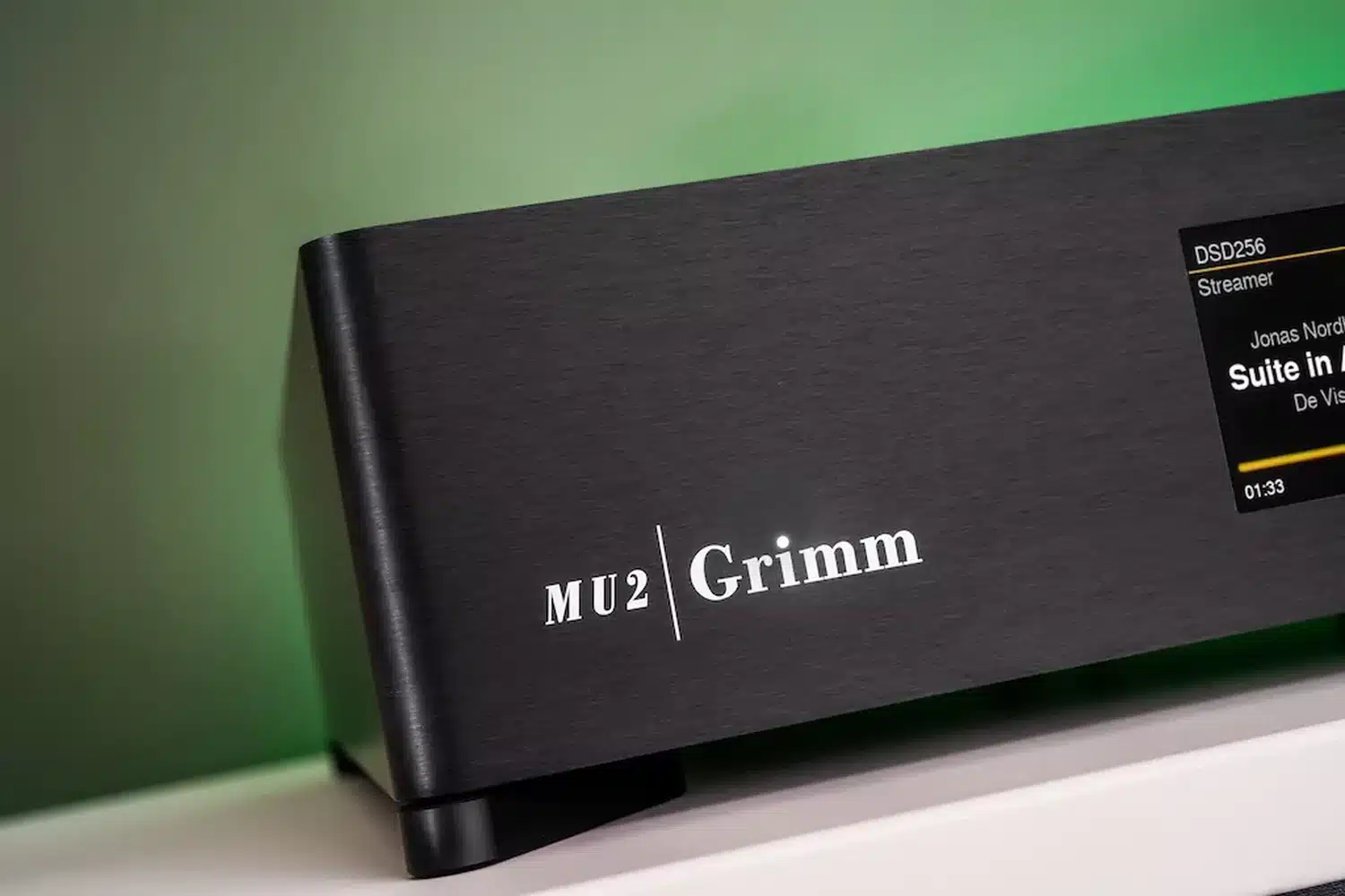 Appareil audiophile, le DAC Grimm Audio MU2 noir est posé sur une étagère blanche avec un mur à fond vert affichant du texte sur son écran "DSD256" (par 1877.audio)