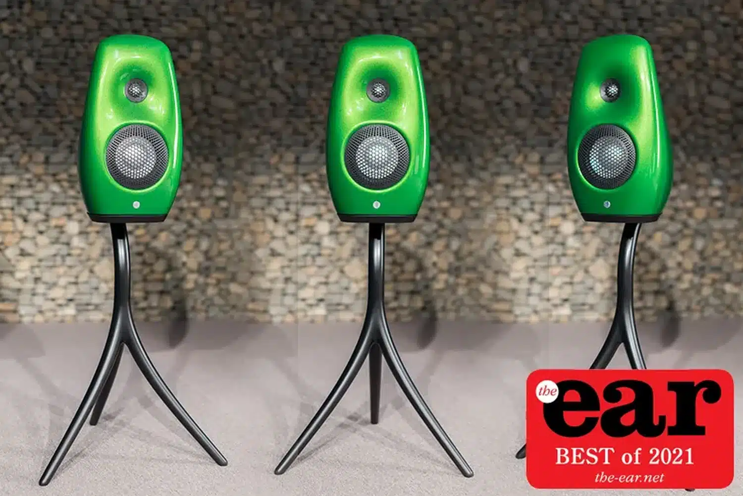 Trois enceintes vertes haut de gamme Vivid Audio Kaya S12 sur leur trépied spécifique se dressent avec des angles différents sur un fond gris en galets avec une étiquette « Best of 2021 » de The Ear (par 1877.audio)