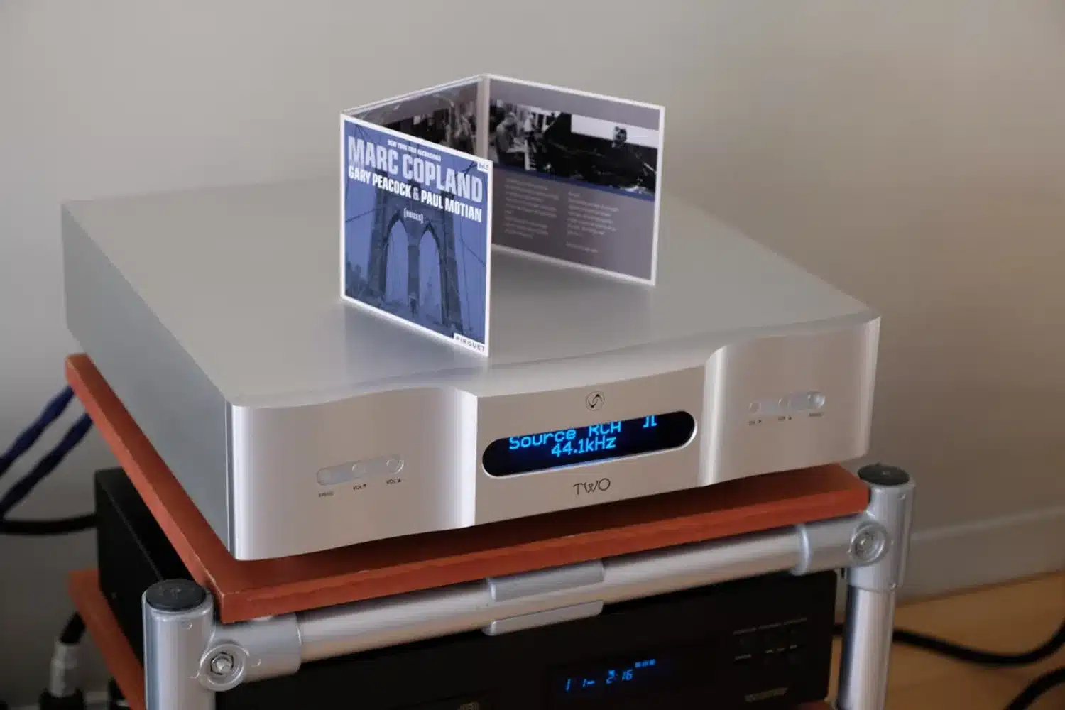 Un DAC Vermeer Audio Two haute résolution affichant « 44,1 kHz » surplombé d'une pochette de CD de l'album de jazz de Marc Copland est placé sur une tablette en bois d'un rack en métal (par 1877.audio)